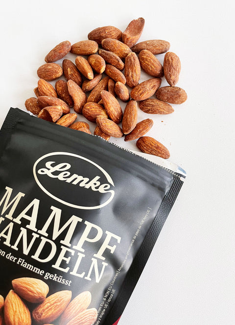 Geröstete Lemke Mampfmandeln neben geöffnetem Beutel auf hellem Hintergrund