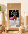 Lemke Mandel Protein 1 kg standing on a wooden countertop in a bright kitchen with whole almonds, a scoop of almond protein powder, and a natural baking setup.