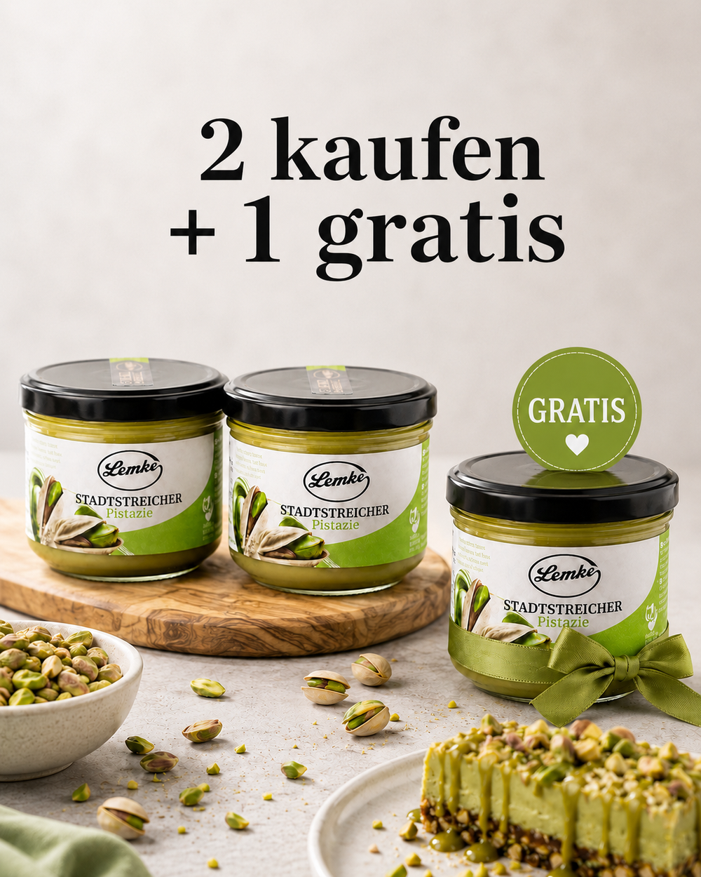 Promotional product image showing three jars of Lemke Stadtstreicher Pistazie pistachio spread on a light background, with two jars on a wooden board and one gift jar with a green ribbon and “Gratis” badge, surrounded by pistachios and a pistachio dessert, plus the headline “2 kaufen + 1 gratis.”
