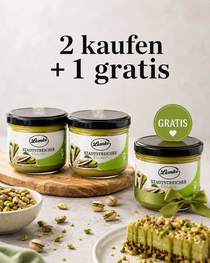 Promotional product image showing three jars of Lemke Stadtstreicher Pistazie pistachio spread on a light background, with two jars on a wooden board and one gift jar with a green ribbon and “Gratis” badge, surrounded by pistachios and a pistachio dessert, plus the headline “2 kaufen + 1 gratis.”
