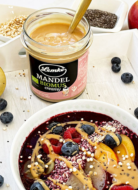 Lemke Mandelcreme Bioprodukt auf einer Smoothie Bowl mit frischen Früchten, Beeren und Chiasamen, auf einem weißen Tablett serviert.